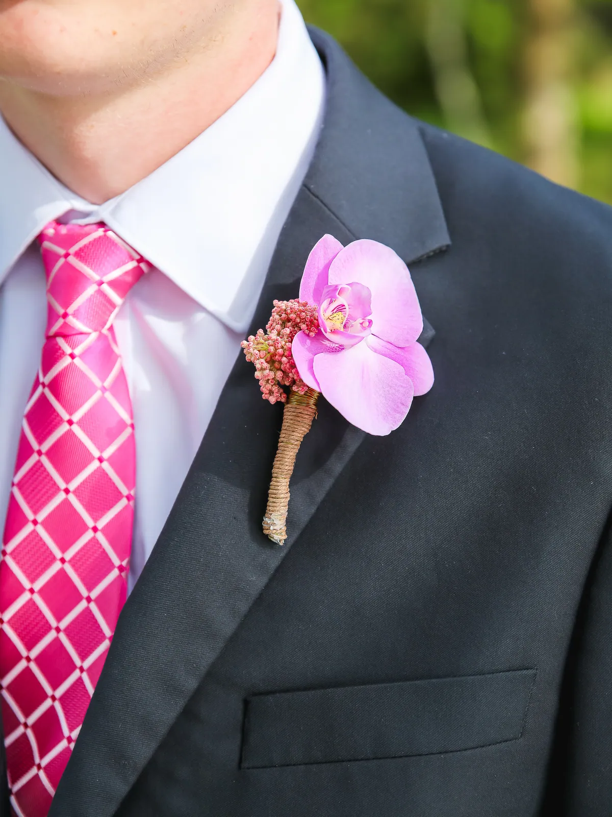 Single pink phalaenopsis orchid boutonniere with a twine-wrapped stem pinned to a charcoal suit lapel