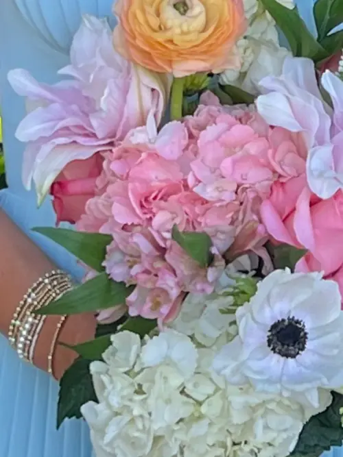 Bouquet of pink hydrangea, white anemones, orange ranunculus and a calla lily against a pale blue gown