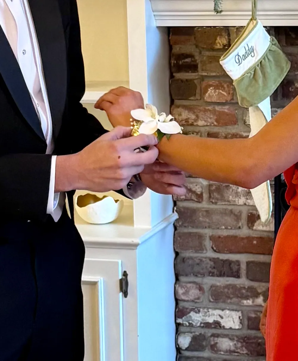 White ranunculus boutonniere being pinned to a black tuxedo lapel