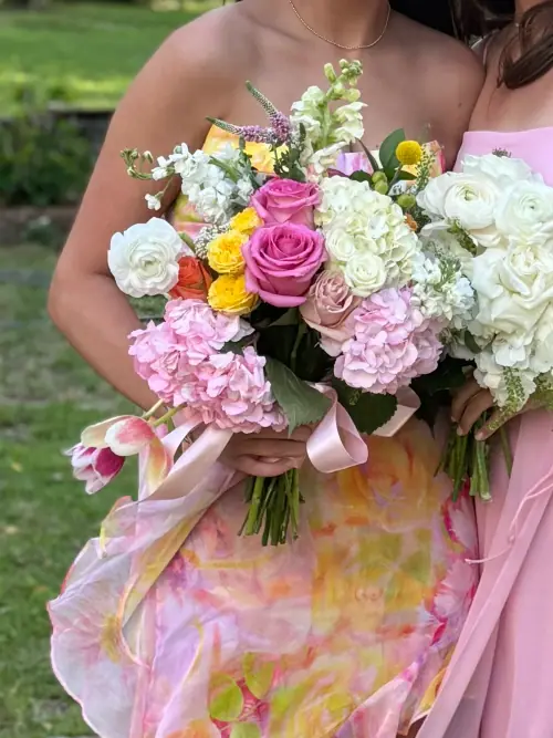 Two bridesmaid bouquets side by side — one of pink and yellow roses, one of white lisianthus and hydrangea