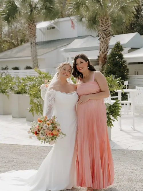Bride holding a peach and coral bouquet of ranunculus and garden roses beside a bridesmaid in a coral gown