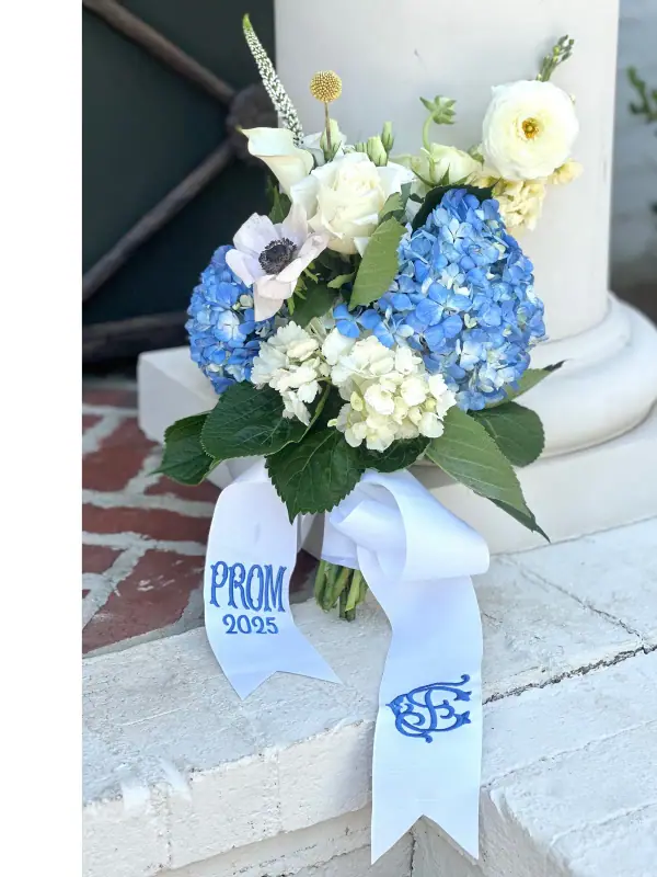 Blue hydrangea, white ranunculus and calla lily bouquet with a monogrammed prom ribbon, set on stone steps
