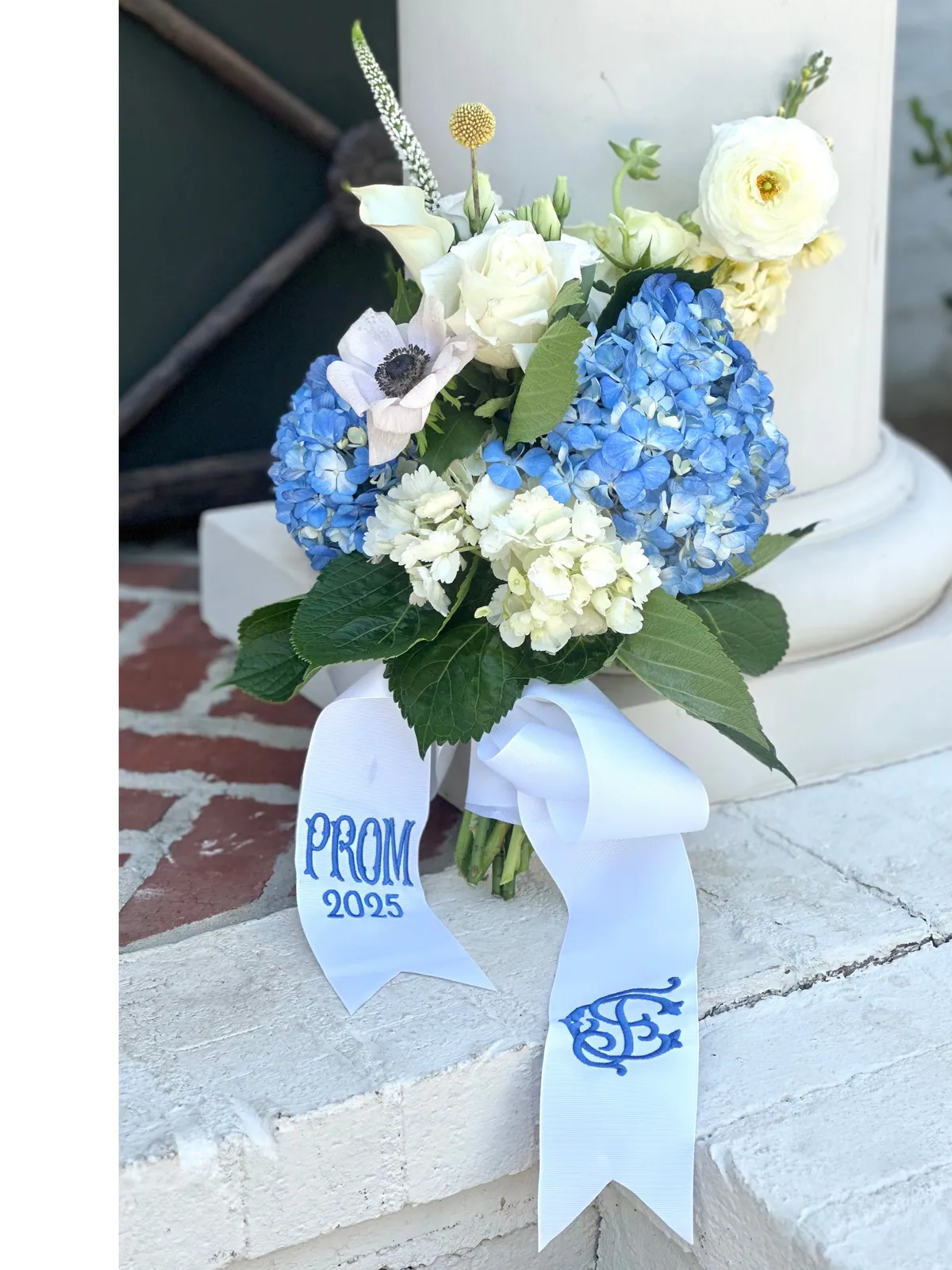 Blue hydrangea, white ranunculus and calla lily bouquet with a monogrammed prom ribbon, set on stone steps